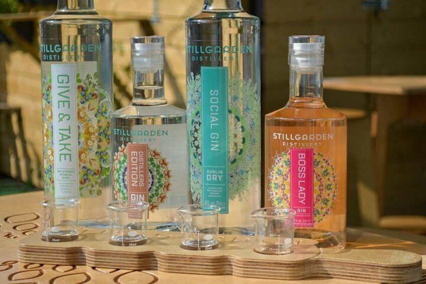 Quatre bouteilles de gin Stillgarden sur une table en bois, avec des piles de pièces de monnaie à côté. 3