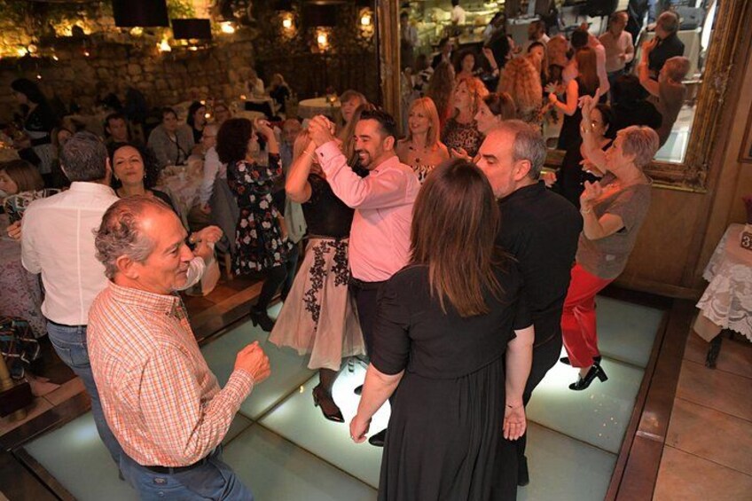 Een groep mensen danst in een ruimte met stenen muren en een spiegel die de scène weerspiegelt. 3