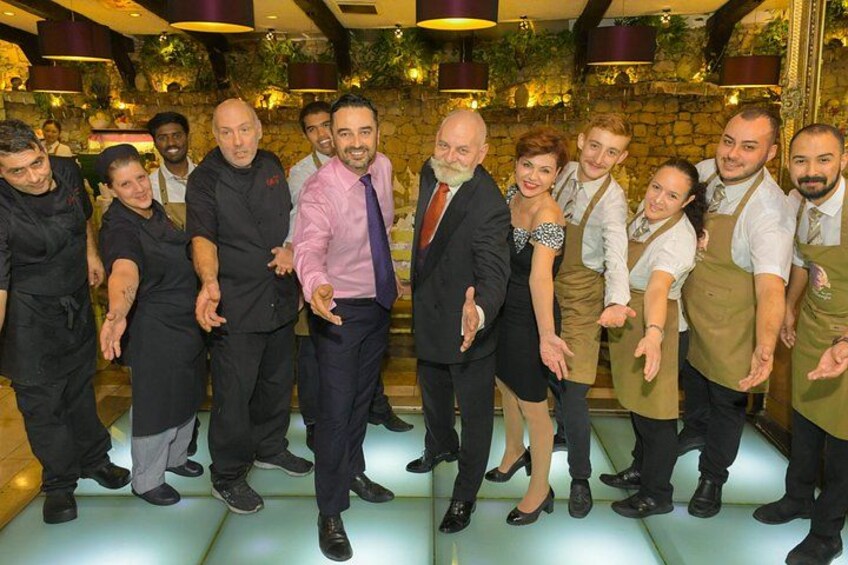 Een groep mensen in een restaurant met een stenen muur en hangende planten op de achtergrond. 2