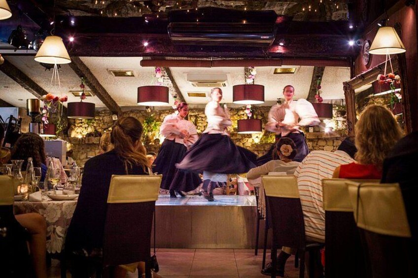 Een restaurant met een podium voor een optreden, tafels met stoelen en een publiek dat toekijkt. 5
