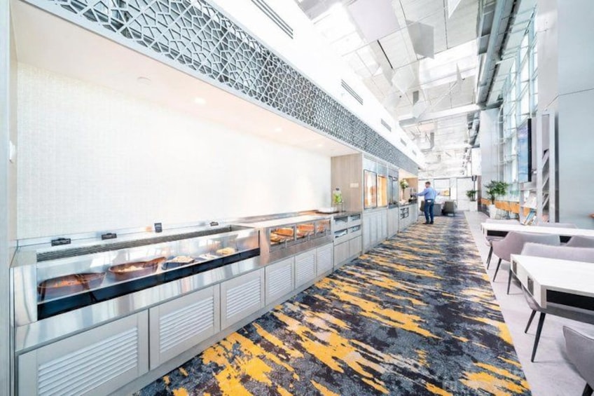 A modern office space with a long counter displaying food items, a patterned carpet, and a person walking in the background. 4