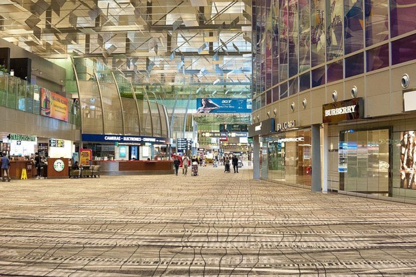 A spacious indoor shopping area with a high ceiling and glass walls, featuring stores like Burberry and Bvlgari. 5