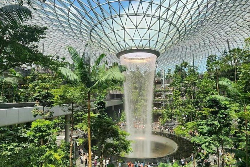 A large indoor space with a glass dome ceiling, a central water feature, and lush greenery. 3