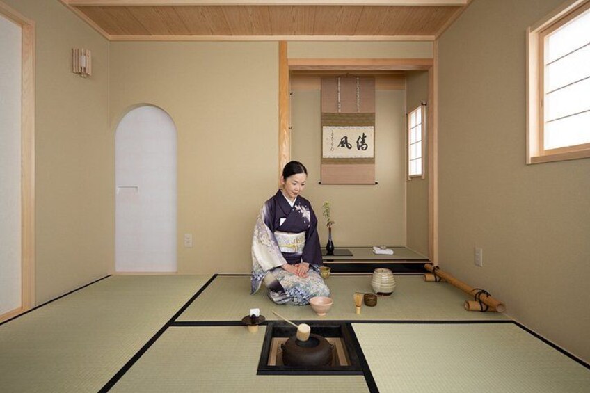Een traditionele Japanse kamer met tatami vloeren, een persoon zittend op de grond, en een shoji scherm op de achtergrond. 2