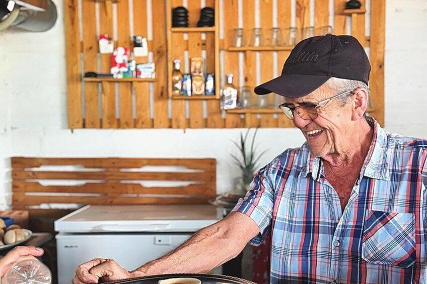 Een oudere man in een geruit shirt en pet, die reikt naar een bakje op een aanrecht. 3
