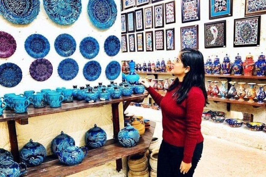 A woman in a red sweater browsing blue pottery on shelves in a store. 4