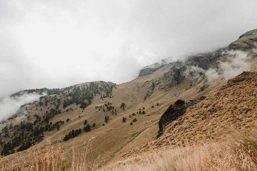 A mountainous landscape with sparse vegetation, rocky terrain, and mist-covered peaks. 5