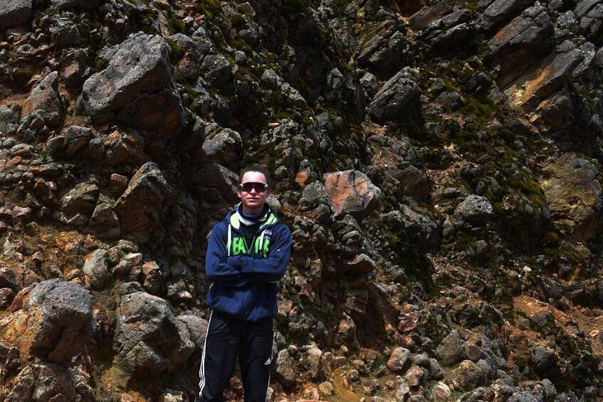 A person standing in a rocky terrain with large boulders and sparse vegetation. 2