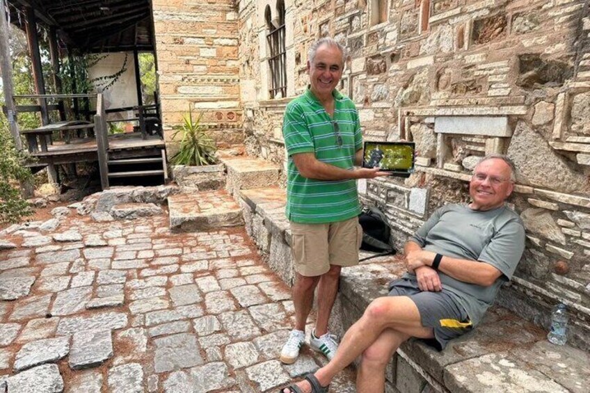 Deux hommes se trouvent dans un cadre extérieur, avec des marches en pierre et un bâtiment à l’aspect rustique. 2