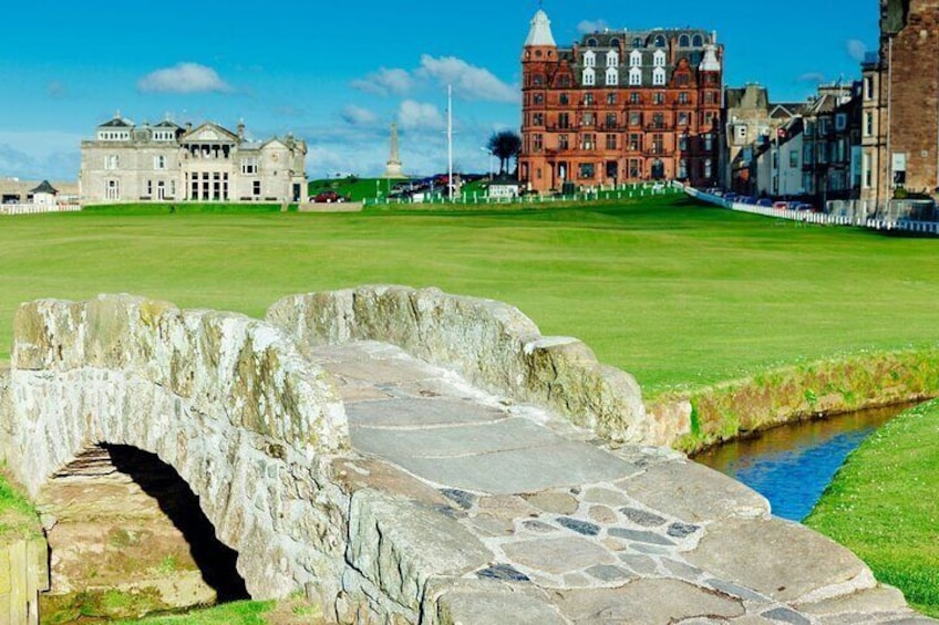 A stone bridge over a canal, a grassy field, and historic buildings in the background. 1