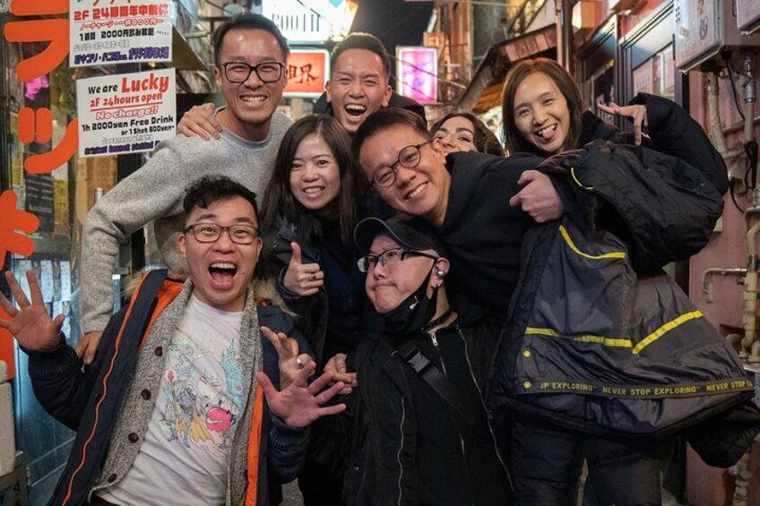 Un groupe de personnes se trouve dans une ruelle d’une ville, entouré de divers panneaux et publicités. 3