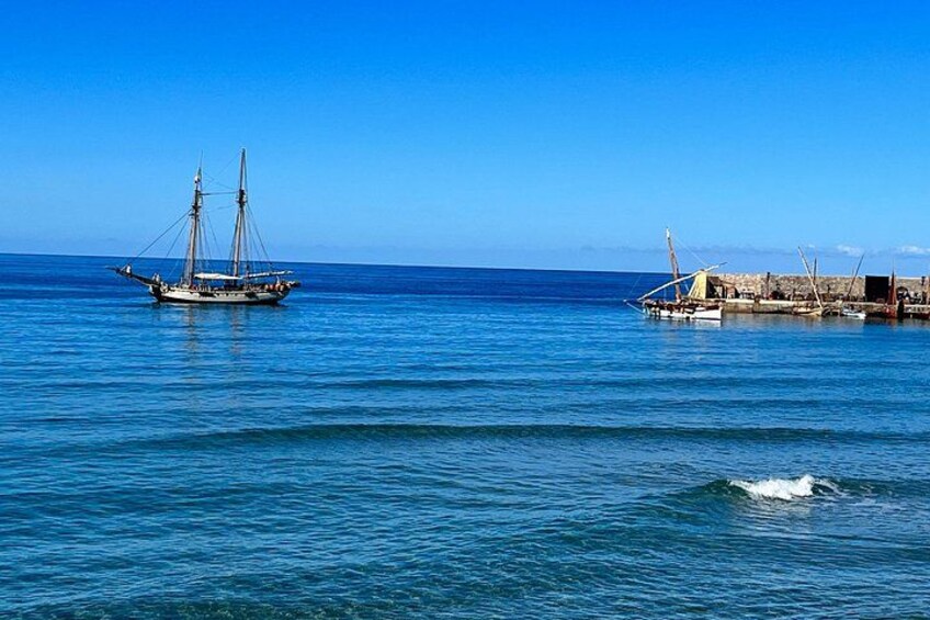Un mar tranquilo con un velero y un muelle con edificios. 5