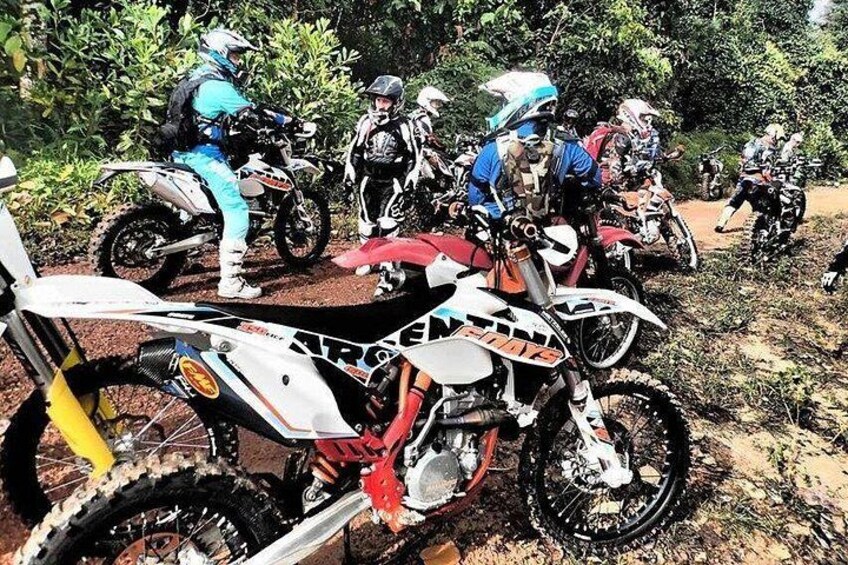 A group of dirt bikes parked on a dirt trail surrounded by greenery. 1