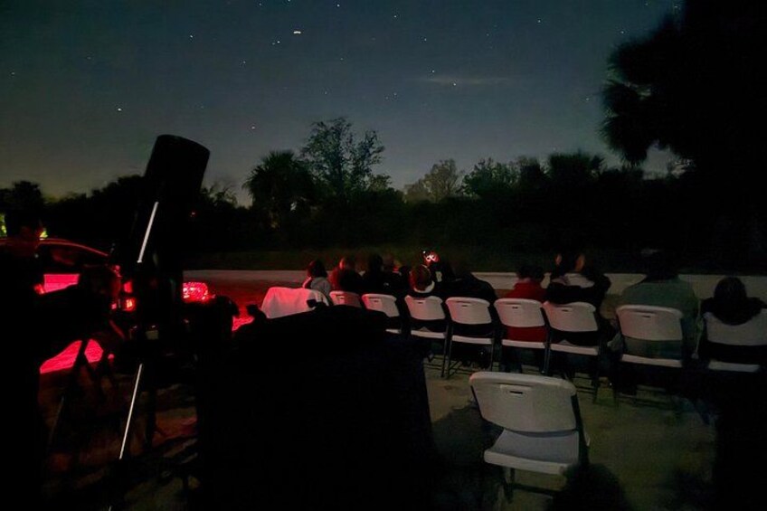 An outdoor event with chairs arranged for attendees, a telescope, and a dark sky with stars. 4