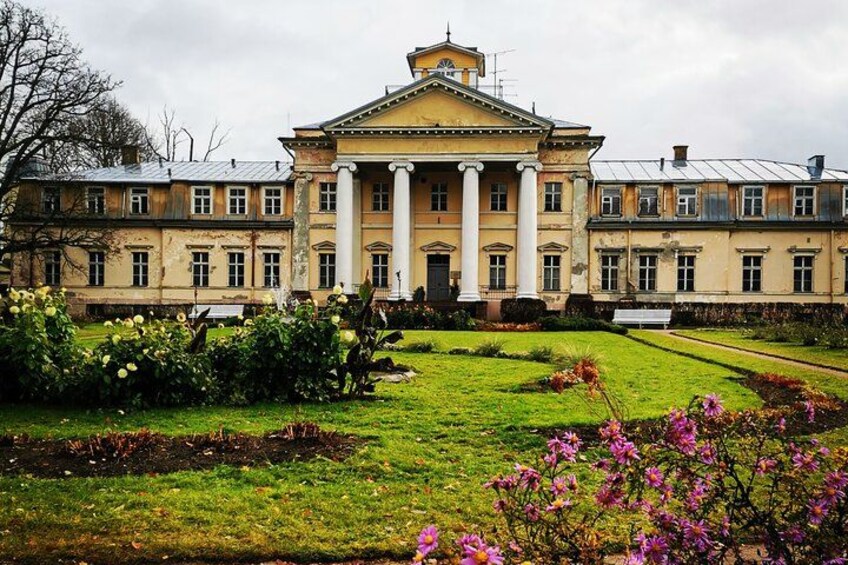 A large classical building with columns, surrounded by a well-maintained garden with various plants and flowers. 3