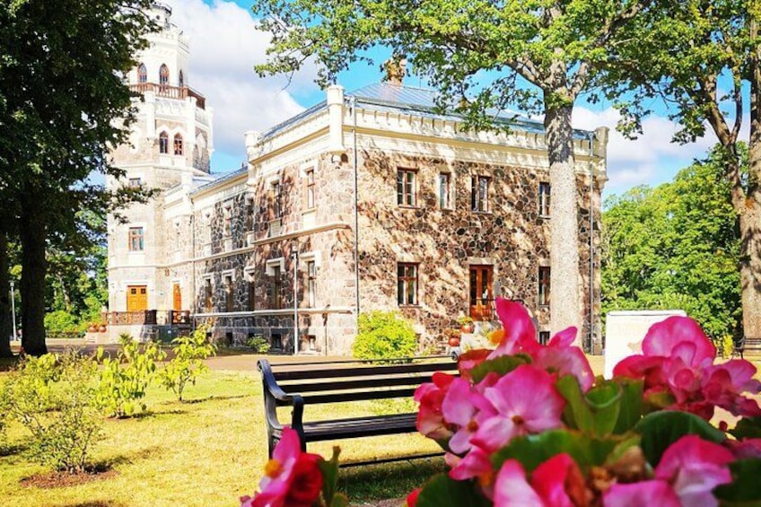 A historic building with a bell tower, surrounded by a well-maintained garden with a bench and vibrant flowers. 4