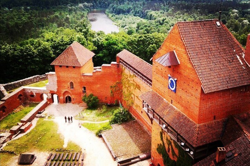 A historic brick castle with a tower, surrounded by lush greenery and a river in the background. 5