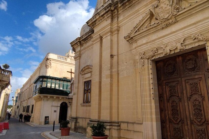 A street with ornate buildings, a large wooden door, and a clear sky. 4