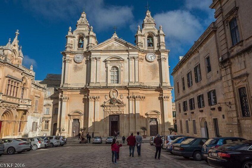 Una iglesia histórica con una torre de campanario, rodeada de coches aparcados y peatones. 4