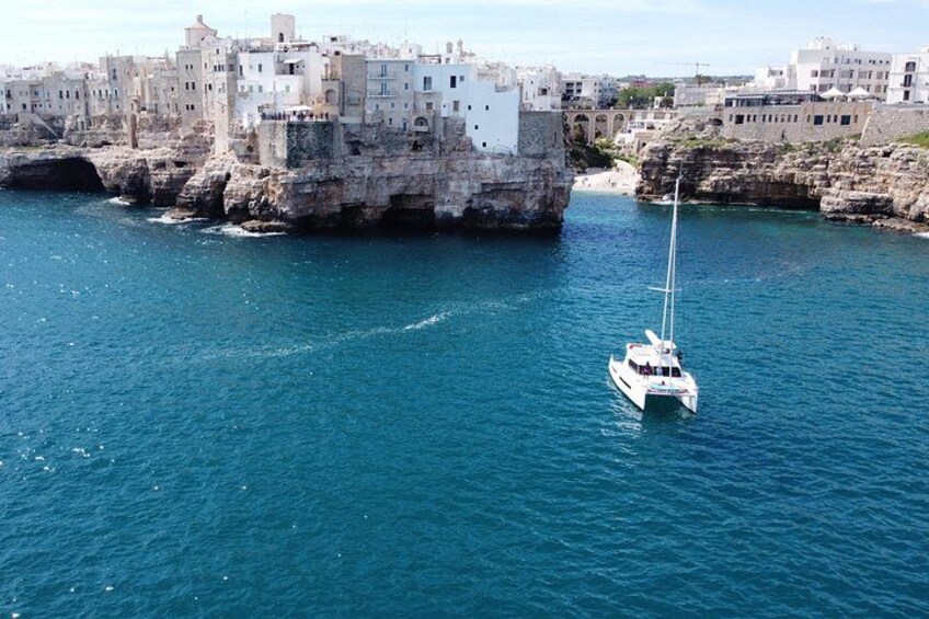 Un voilier sur une mer calme, une côte rocheuse et des bâtiments en arrière-plan. 2