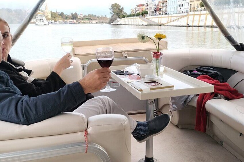 Una persona relajándose en un barco con una mesa, sosteniendo una copa de vino tinto y un jarrón con flores. 2