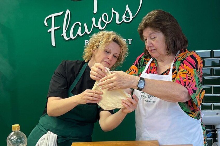 Two people preparing food, one wearing a green apron and the other in a colorful shirt, with a green wall in the background. 4