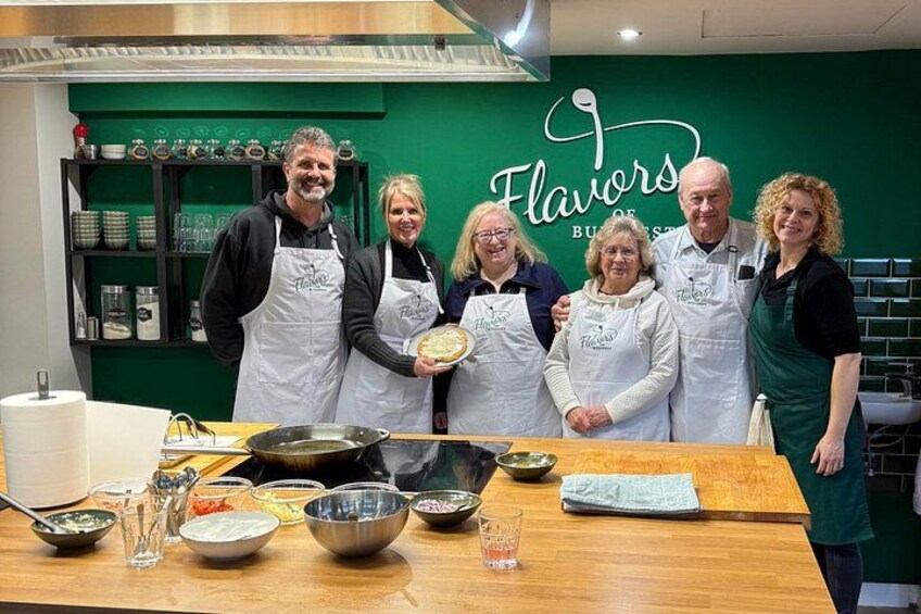 A group of people in a kitchen with a green wall and shelves of kitchenware. 1