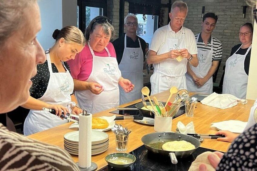 A group of people wearing aprons, engaged in cooking activities around a table with cooking utensils and ingredients. 5