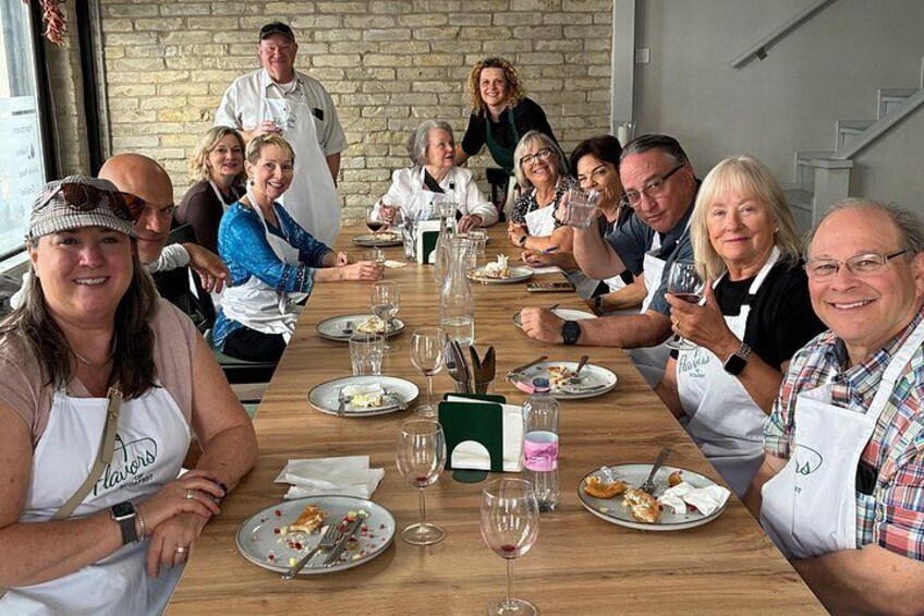 A group of people seated around a long wooden table, engaged in a meal with plates of food and wine glasses. 5