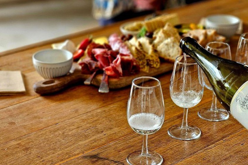 Ein Holztisch mit drei Weingläsern, einer Champagnerflasche und verschiedenen Speisen, darunter Brot und Fleisch. 5