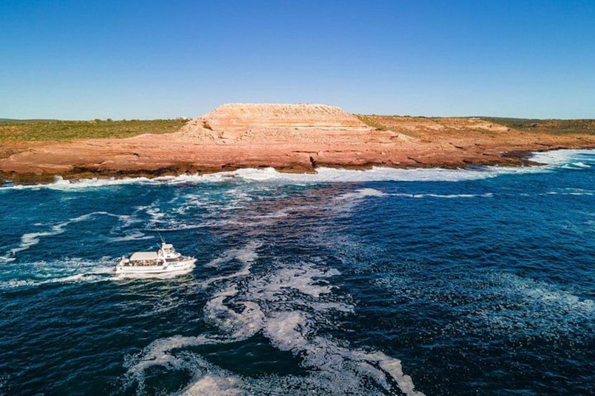 A boat on a body of water with a rocky coastline in the background. 1