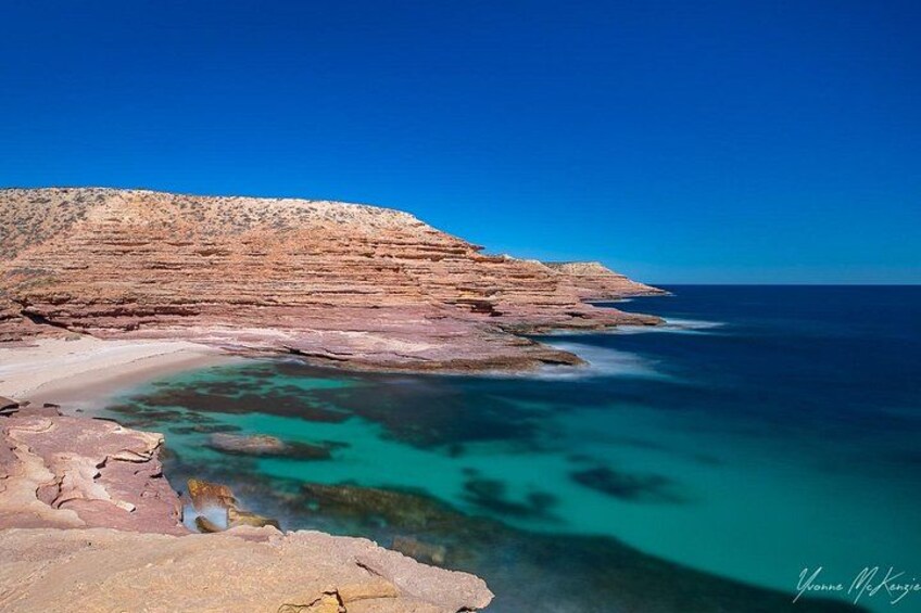 A coastal landscape with layered rock formations and clear turquoise waters. 4
