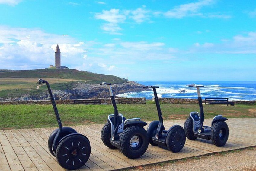 Tre segways på et trædæk ved havet med et fyrtårn i baggrunden. 1