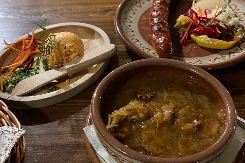 A wooden table with a bowl of stew, a sausage, a plate with a salad, and a bun. 2