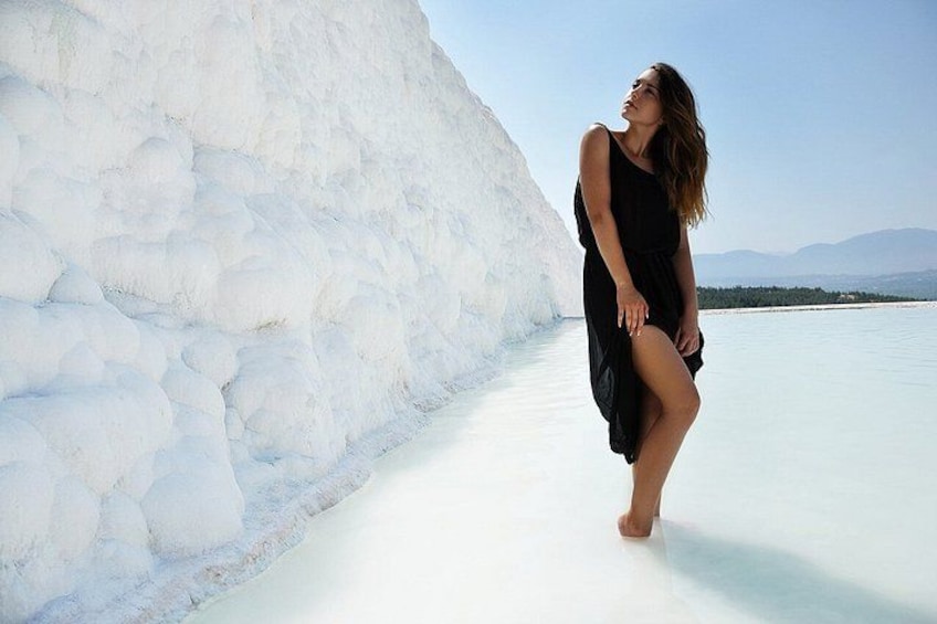 Une personne vêtue d’une robe noire se tient sur une surface blanche, avec une grande formation rocheuse blanche en arrière-plan. 2