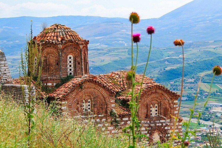 A historical building with arched windows and a tiled roof, surrounded by a mountainous landscape. 2