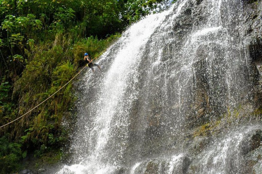 Iemand abseilt een waterval, omringd door weelderige begroeiing. 2