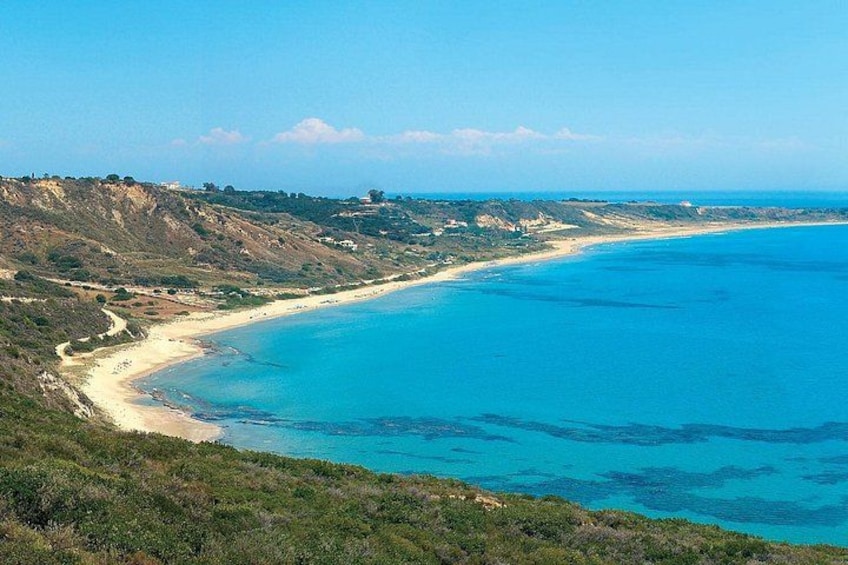 A coastal landscape with a sandy beach, clear blue waters, and hilly terrain. 4