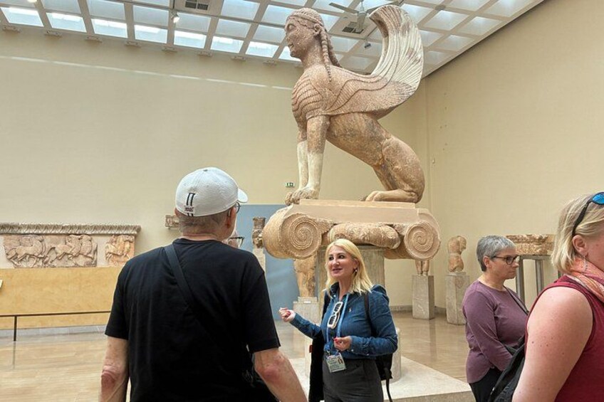 L’intérieur d’un musée où des visiteurs observent une grande sculpture de style classique. 1