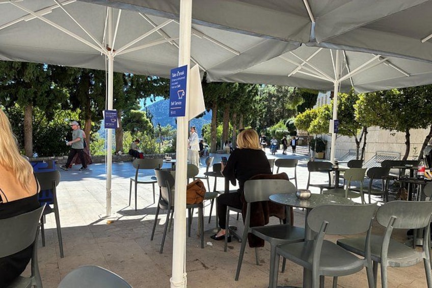 Un café en plein air avec des tables et des chaises disposées sous une marquise, entouré d’arbres. 3
