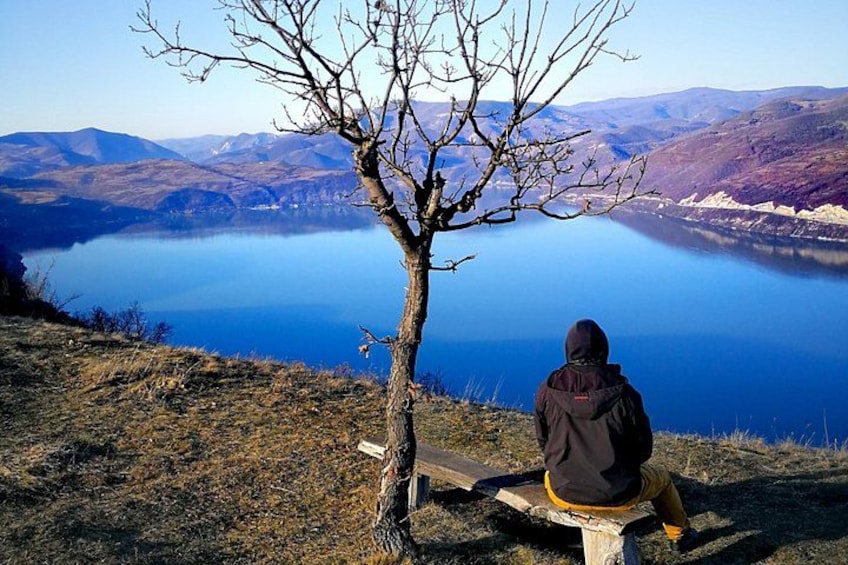 Una persona sentada en un banco mirando un lago con montañas al fondo. 5