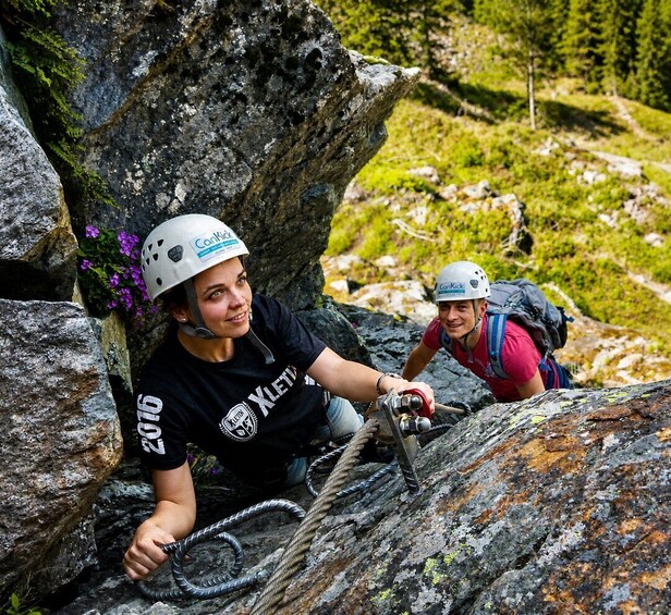 Two people climbing a rocky mountain with ropes, wearing helmets, and hiking gear. 2