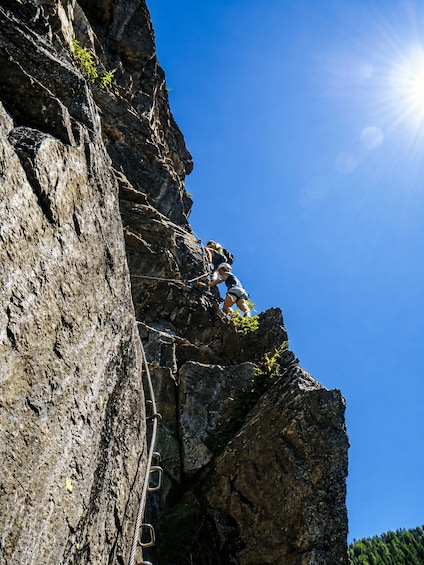A person climbing a rocky cliff with a rope. 3