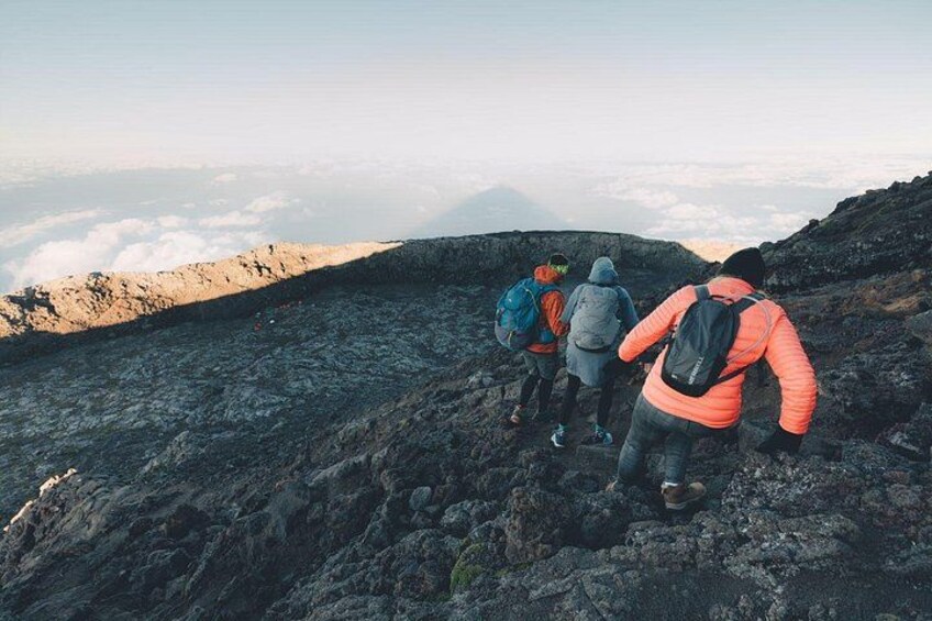 A group of hikers on a rocky mountain trail with a view of clouds and distant mountains. 3