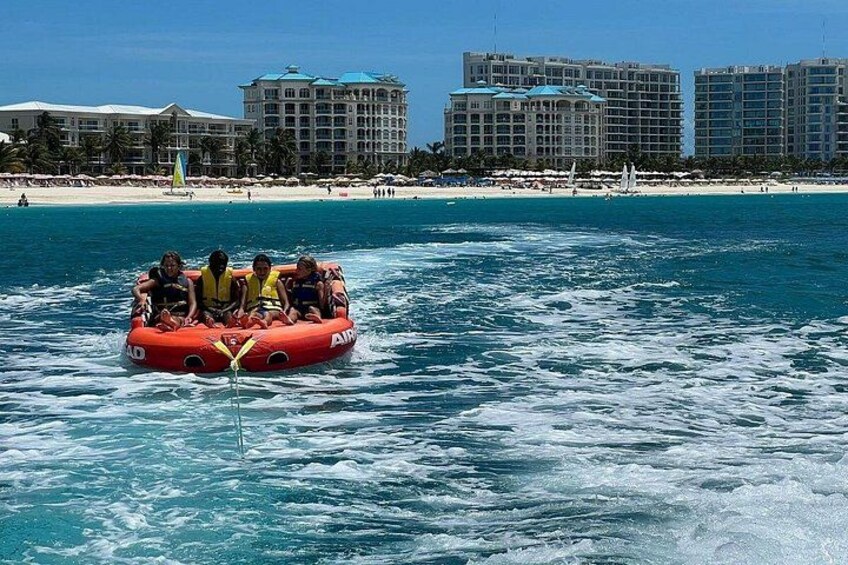 A group of people on a red inflatable raft in the ocean, with a beach and hotels in the background. 5