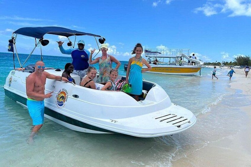 A group of people on a boat near a beach with other boats and people in the background. 4