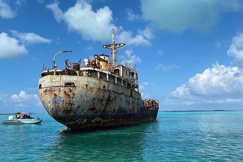 A rusted shipwreck in clear blue waters with a small boat nearby. 3