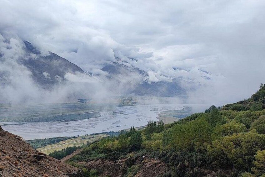A mountainous landscape with a valley, dense forest, and a lake partially obscured by clouds. 4
