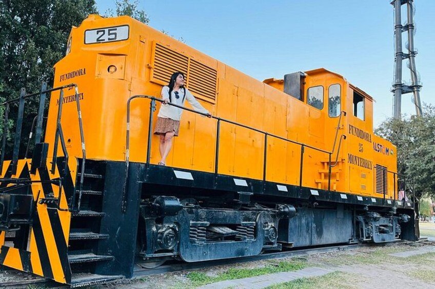 Een gele treinlocomotief met het nummer 25, voorzien van de aanduidingen 'FUNDORA' en 'MONTERREY', staat geparkeerd op rails met een ladder en een persoon die erop staat. 2