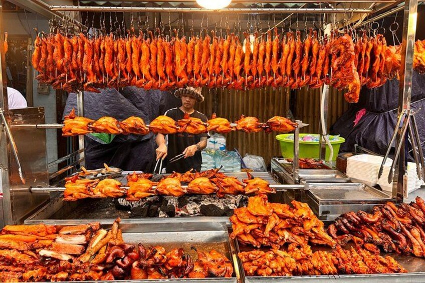 Un vendedor de comida callejera preparando y mostrando pollos asados y otras carnes. 2